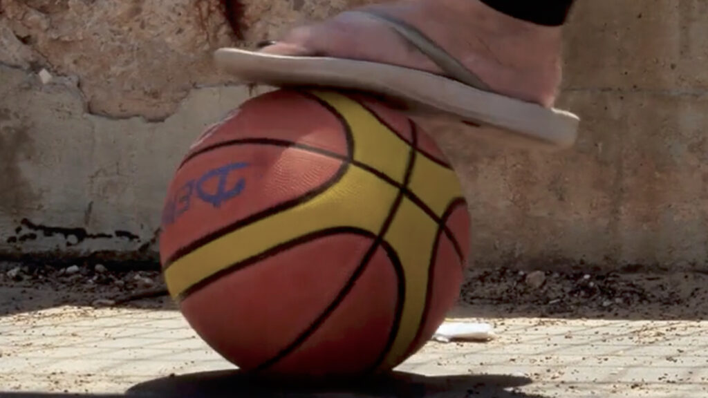 Basketball resting on ground near foot, outdoor court