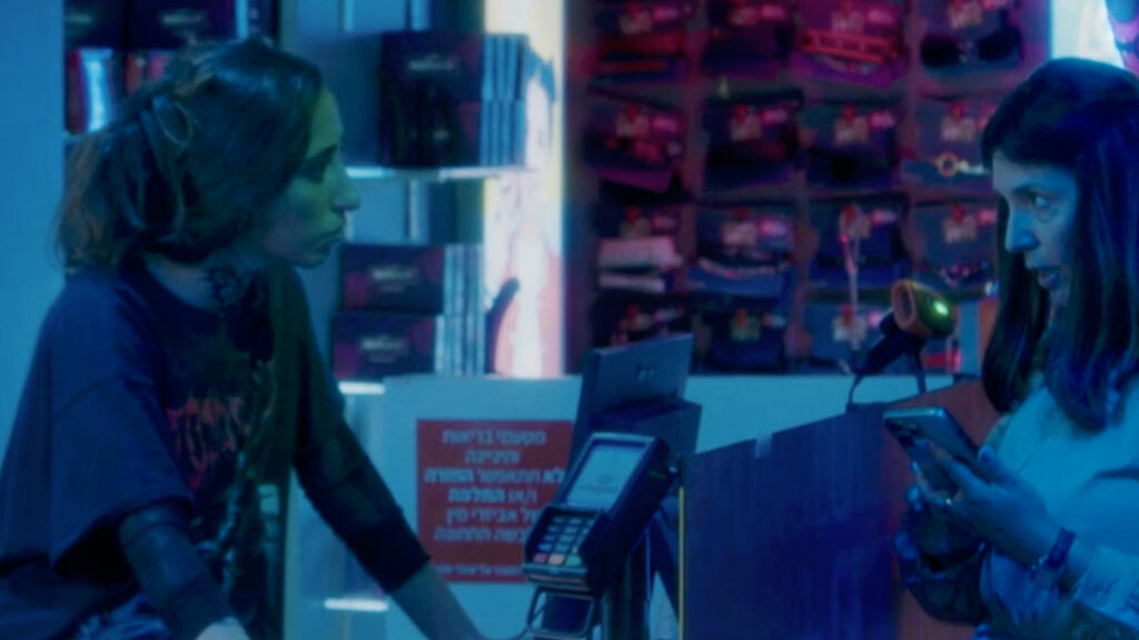 Woman speaking to shop worker across counter in neon-lit retail space