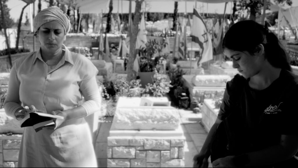Two women standing beside grave in cemetery, black and white wide shot
