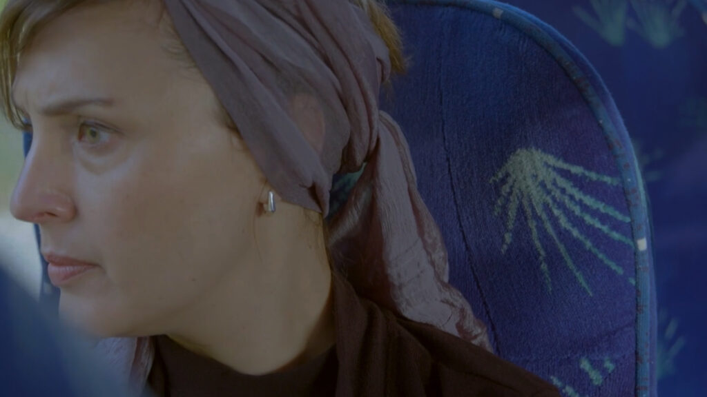 Woman in headscarf sitting on bus, profile view, looking right, soft daylight